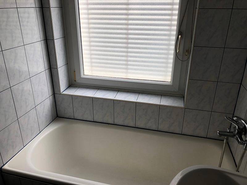 Nahaufnahme der Badewanne und des Fensters im gefliesten Badezimmer.