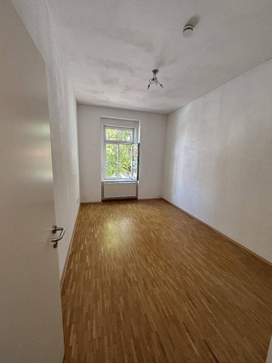 Helles Zimmer mit Parkettboden, weiß gestrichenen Wänden und einem Fenster.