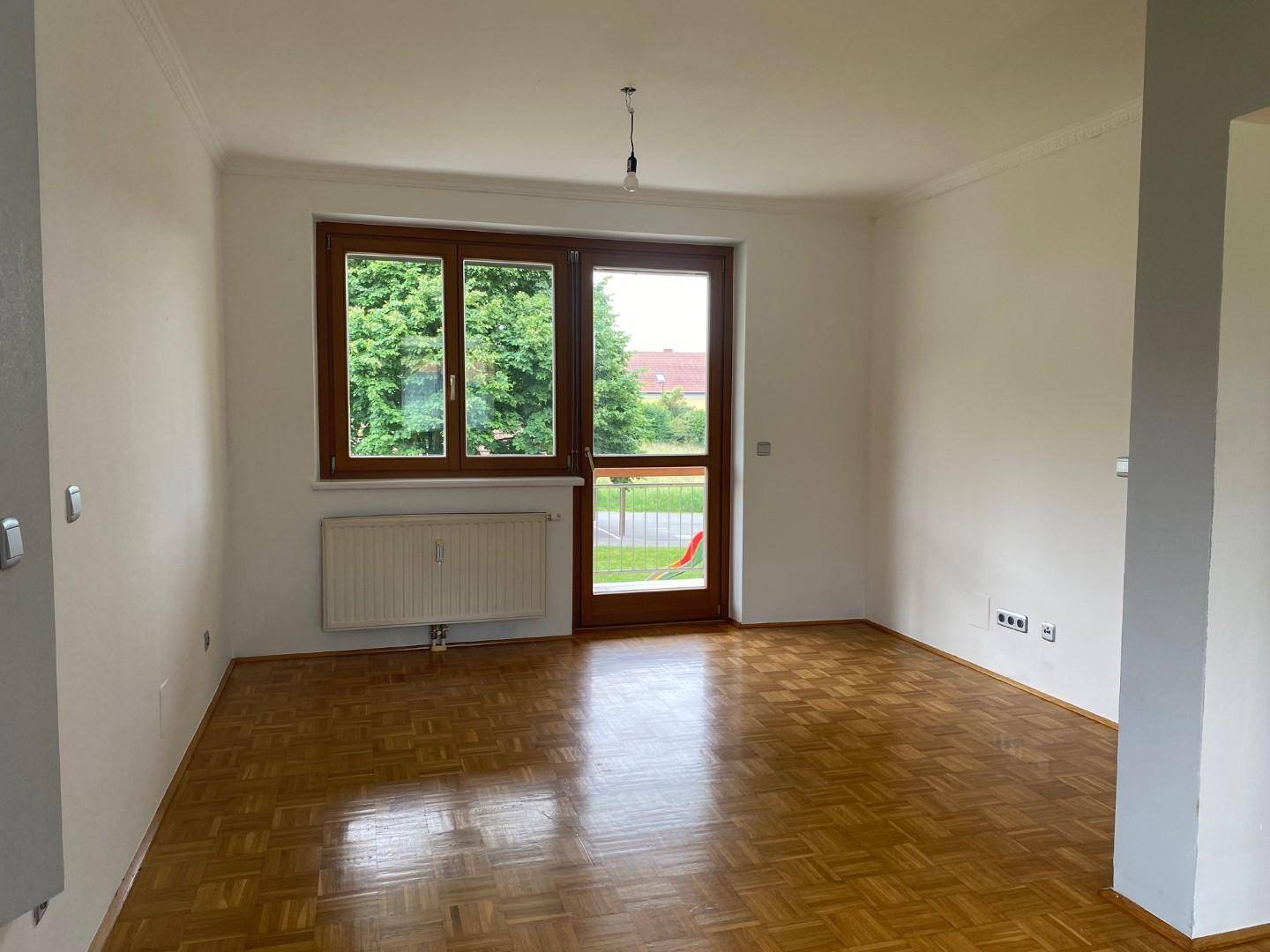 Geräumiges Wohnzimmer mit Parkettboden, weiß gestrichenen Wänden und Balkonzugang.