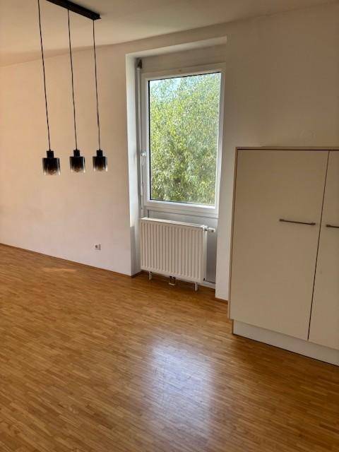 Heller Wohnbereich mit Parkettboden, großem Fenster und moderner Pendelleuchte.