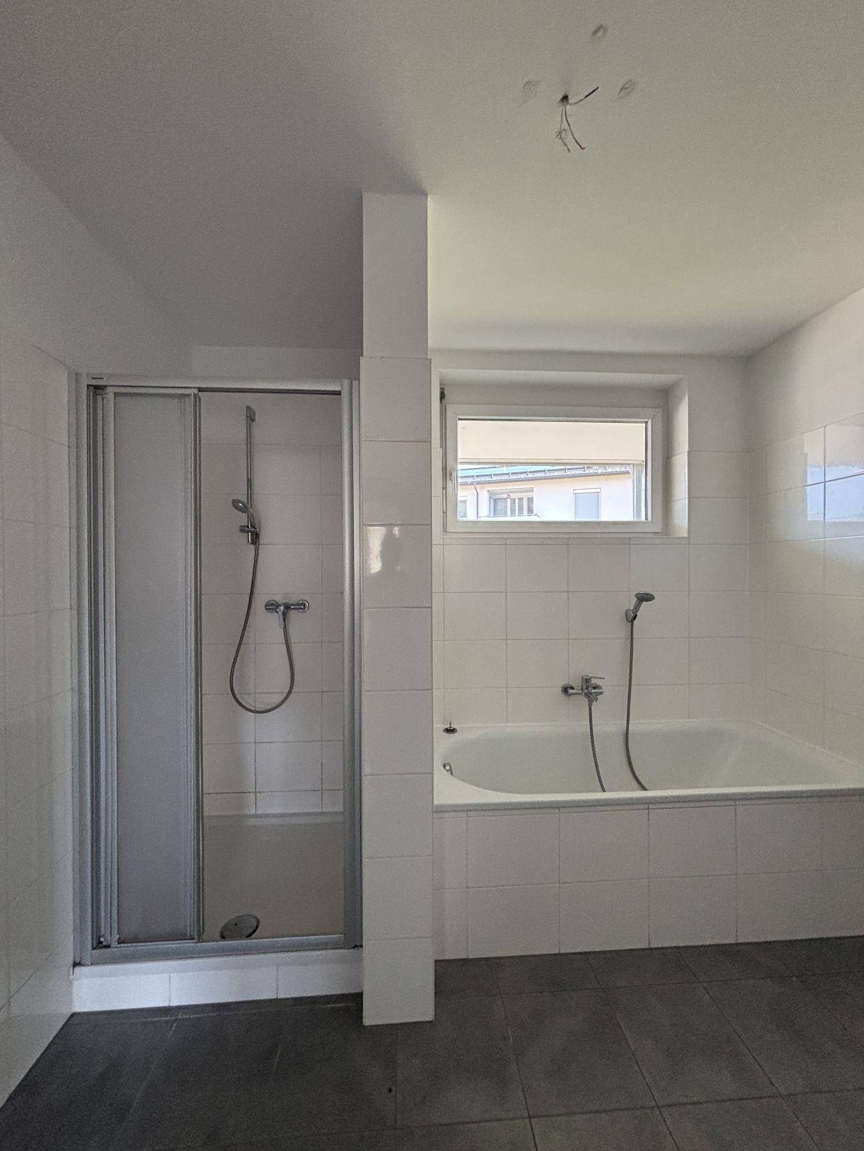 Modernes Badezimmer mit weißen Fliesen, Badewanne, Duschkabine und einem Fenster für Tageslicht.