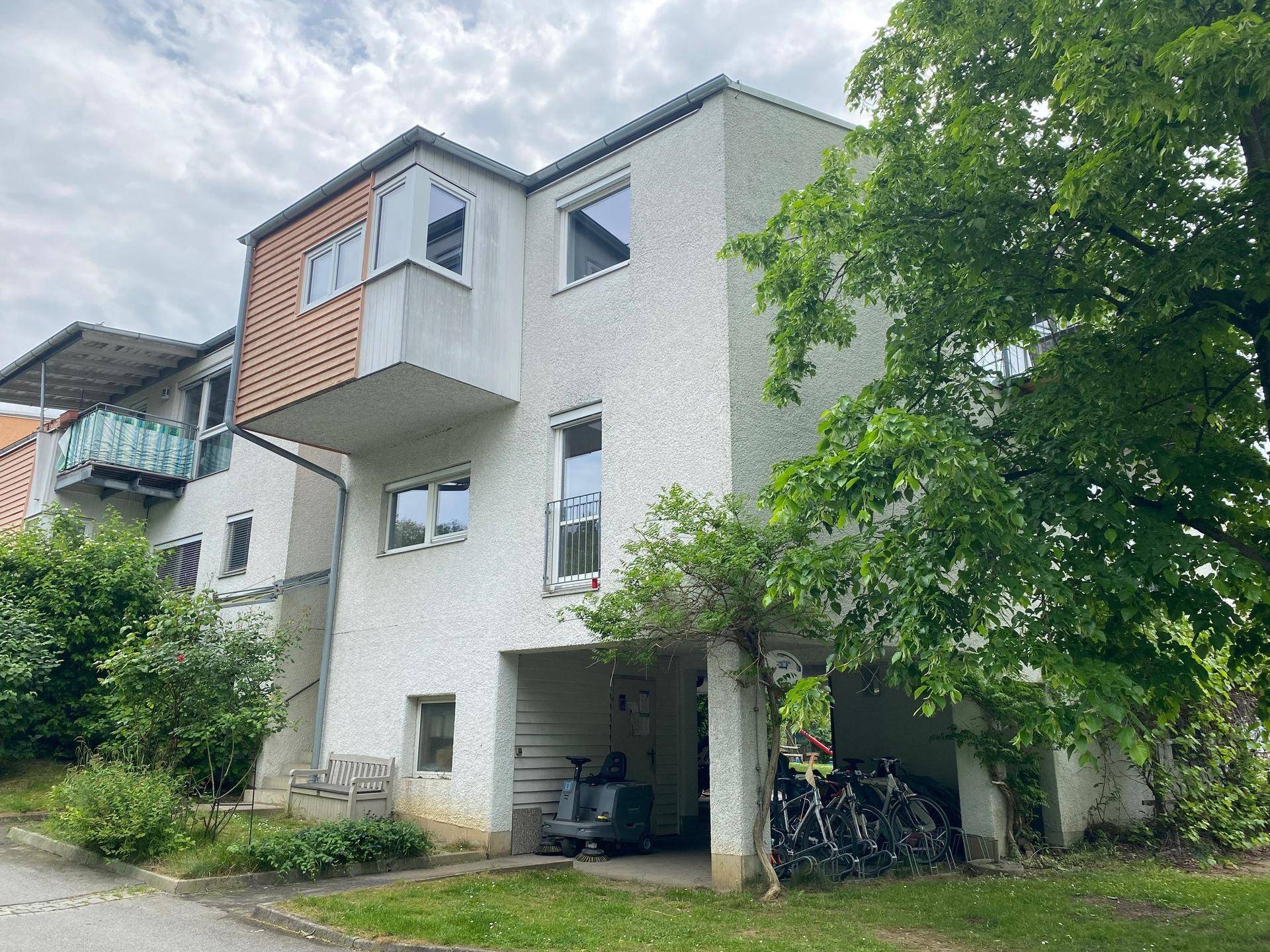 Fassade eines Wohngebäudes mit Holzelementen, Fenstern und einem überdachten Bereich für Fahrräder.