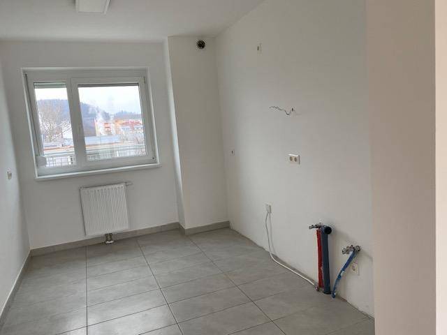 Leerer Küchenraum mit Fliesenboden, Fenster und vorbereiteten Anschlüssen für die Küche.