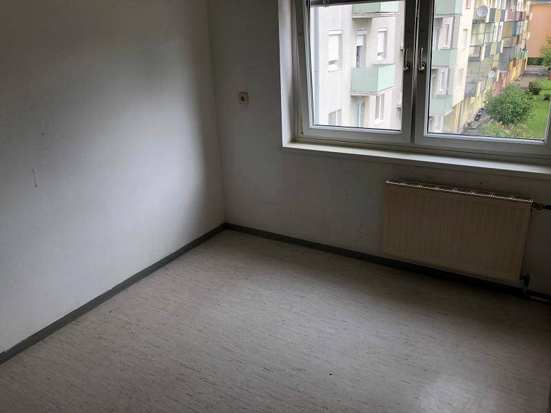 Leeres Zimmer mit Fensterblick auf umliegende Gebäude und Heizkörper.