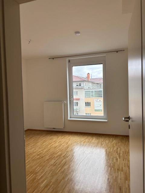 Helles Zimmer mit Parkettboden und Fenster, das einen Ausblick auf die umliegende Bebauung bietet.