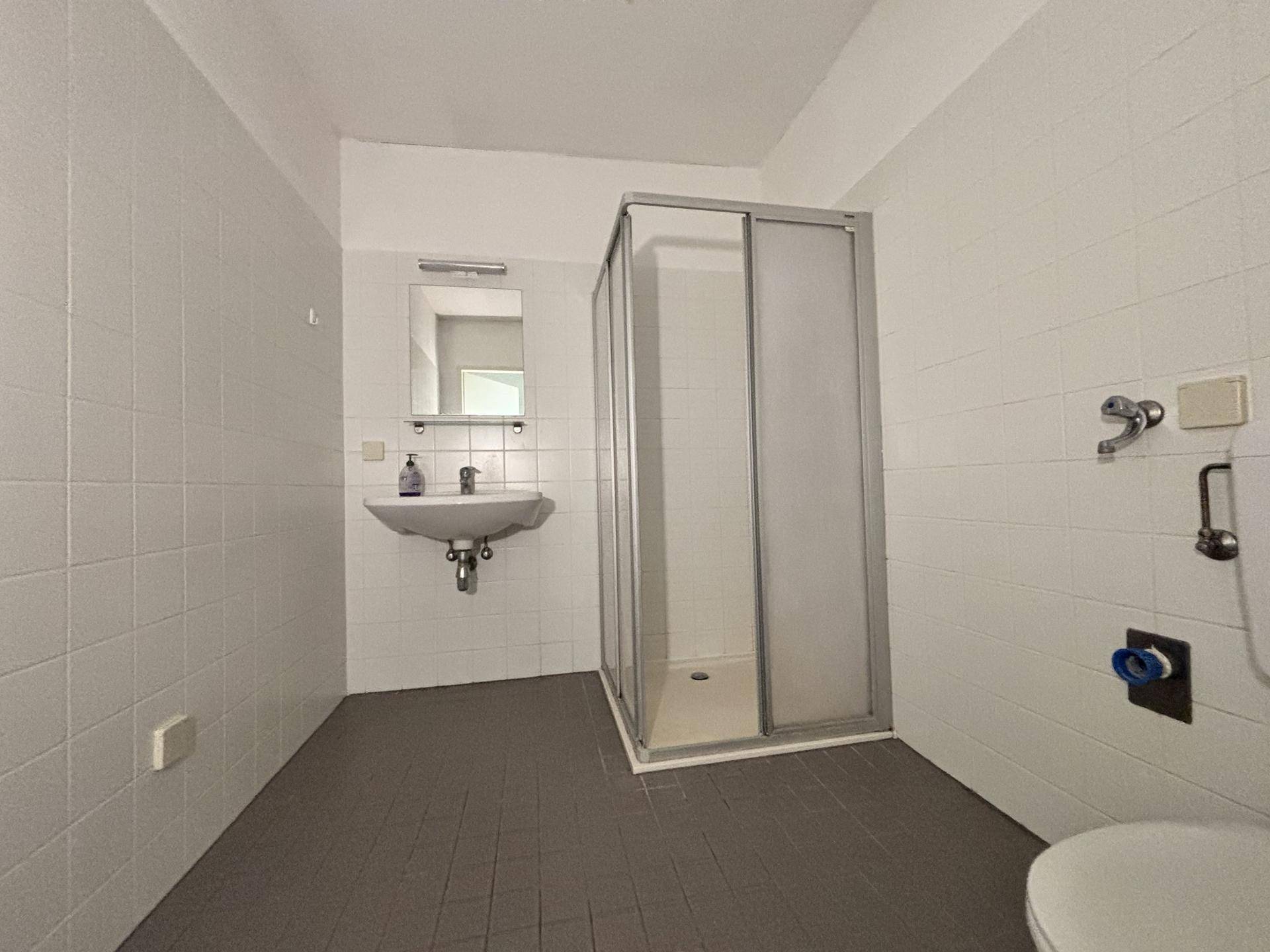 Badezimmer mit Duschkabine, Waschbecken und weißen Fliesen an den Wänden.