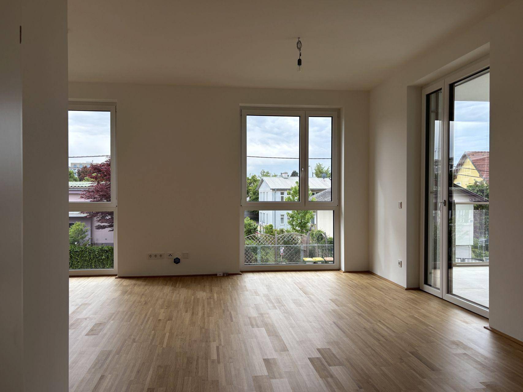 Lichtdurchflutetes Zimmer mit Parkettboden und großen Fenstern mit Blick ins Grüne.