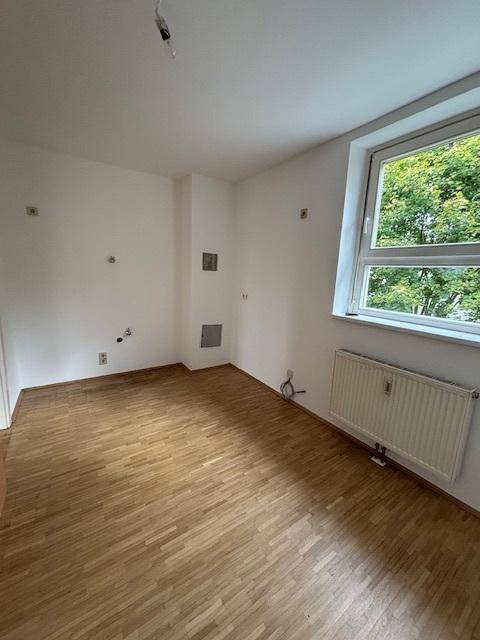 Schlafzimmer mit Parkettboden und großem Fenster, das viel Licht hereinlässt.