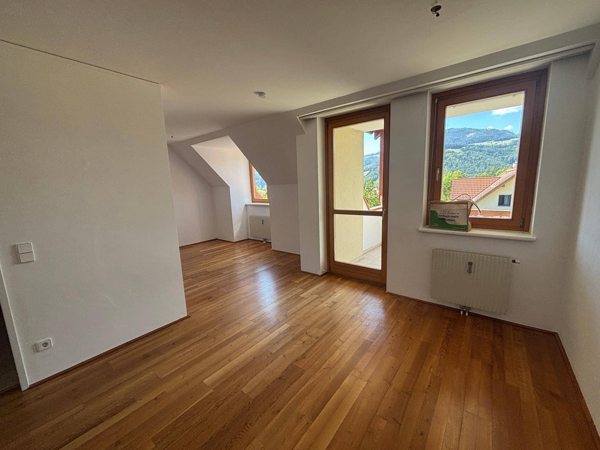 Heller Wohnraum mit Holzparkett, Dachschrägen und Zugang zu einem Balkon mit Bergblick.
