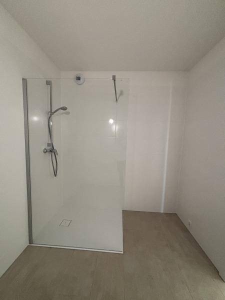 Modernes Badezimmer mit ebenerdiger Dusche und Glasabtrennung, hell gefliest.