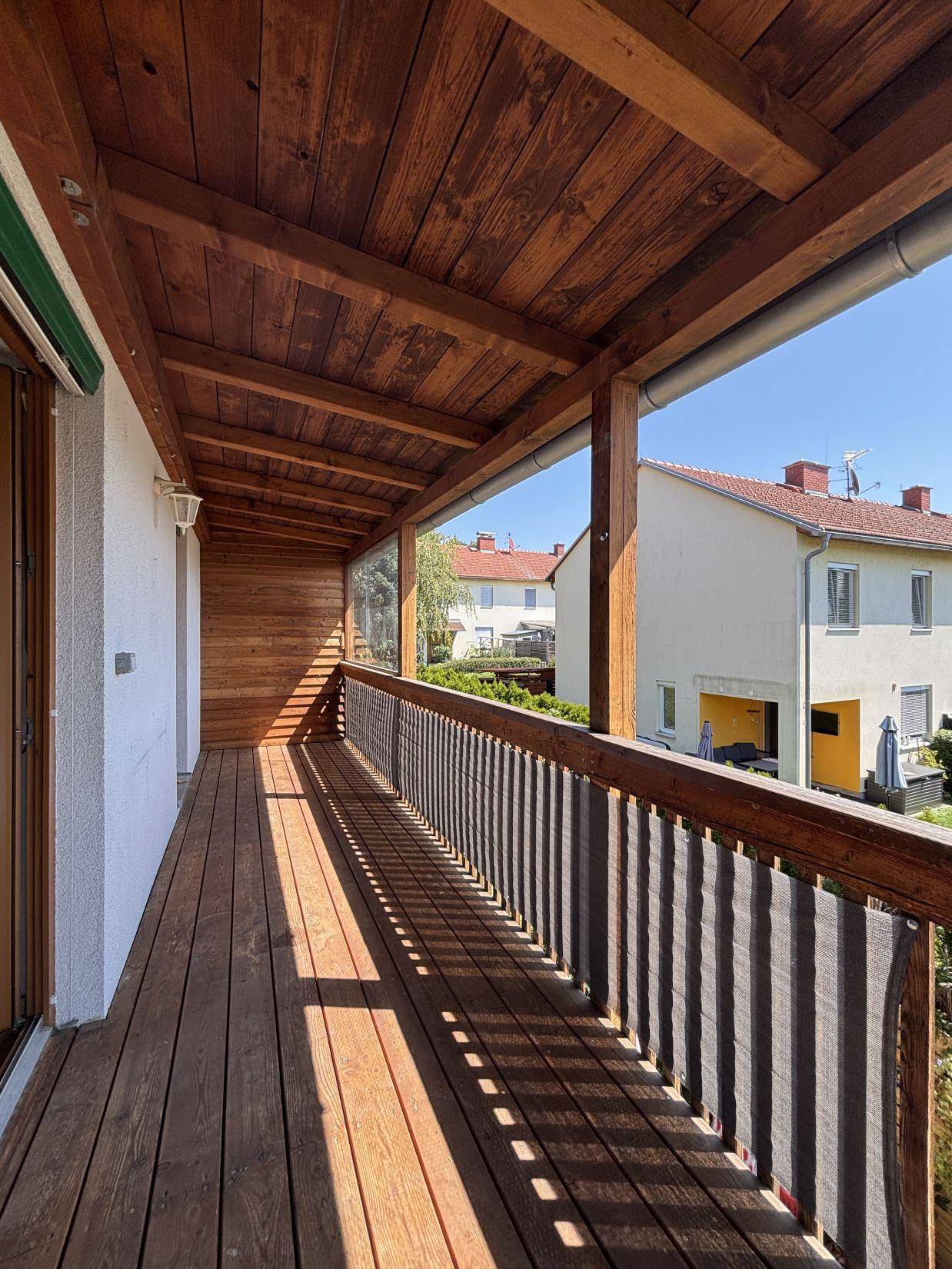 Überdachter Balkon mit Holzverkleidung und Blick auf die umliegenden Häuser und Gärten.