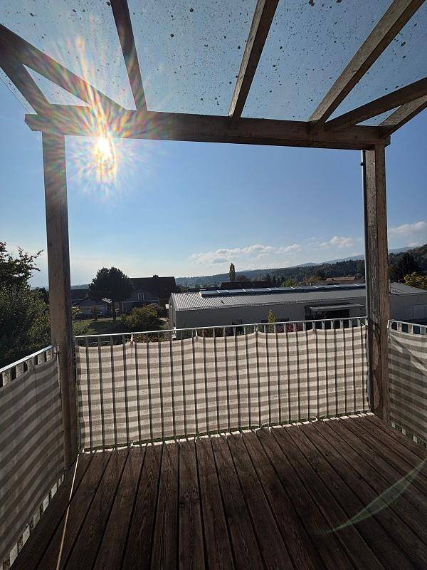 Sonniger Balkon mit Holzboden und Pergola, bietet einen weiten Blick über die Landschaft.