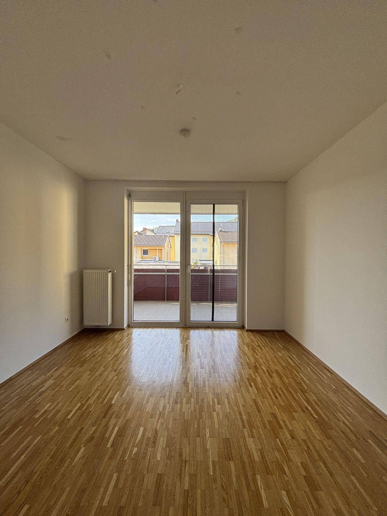 Lichtdurchflutetes Zimmer mit Parkettboden und direktem Zugang zu einem sonnigen Balkon.