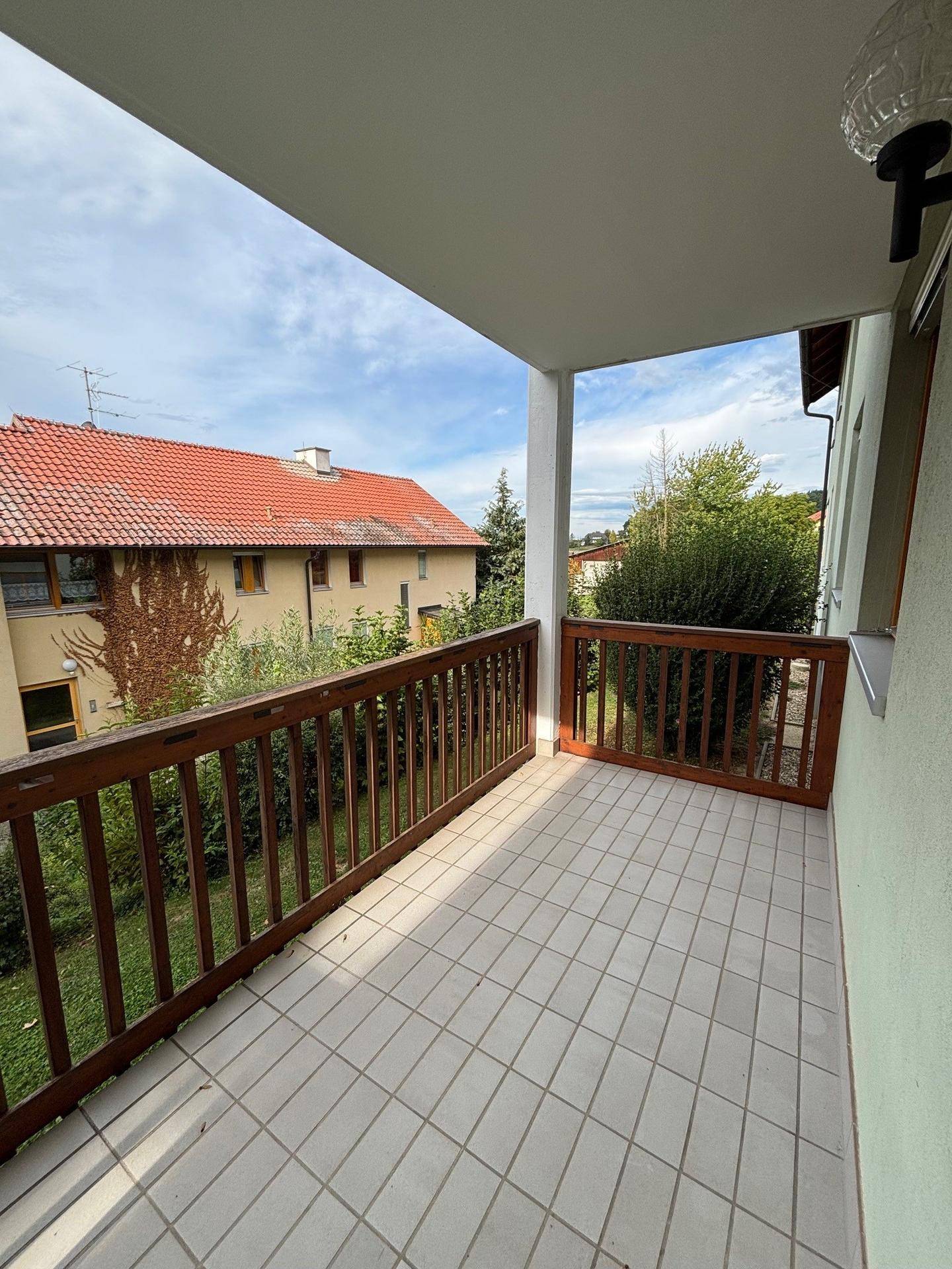 Balkon mit Fliesenboden und Holzgeländer bietet Blick auf die umliegenden Häuser und viel Grün.