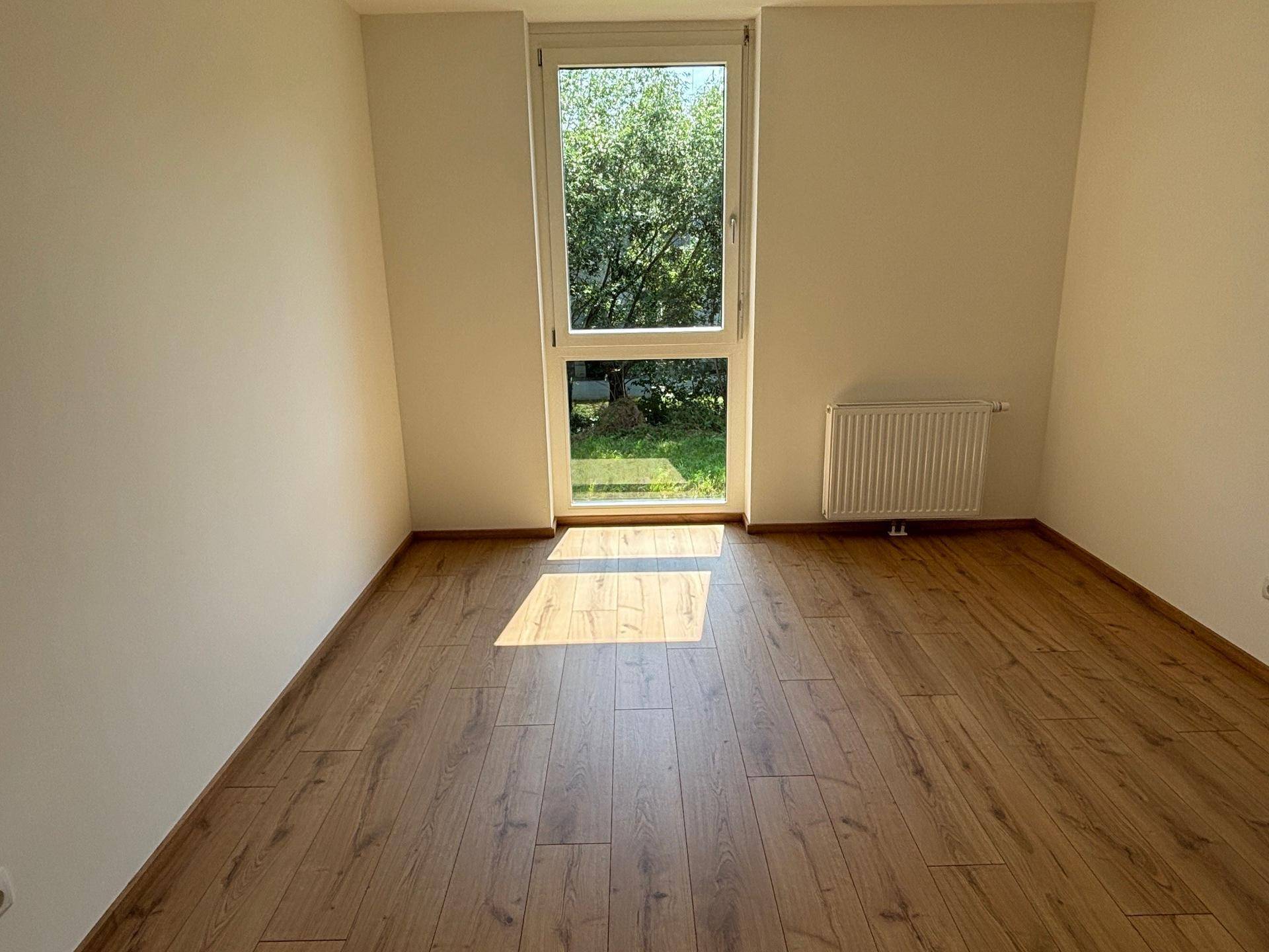 Helles Zimmer mit Laminatboden, weißen Wänden und Blick ins Grüne, ideal als Schlaf- oder Arbeitszimmer.