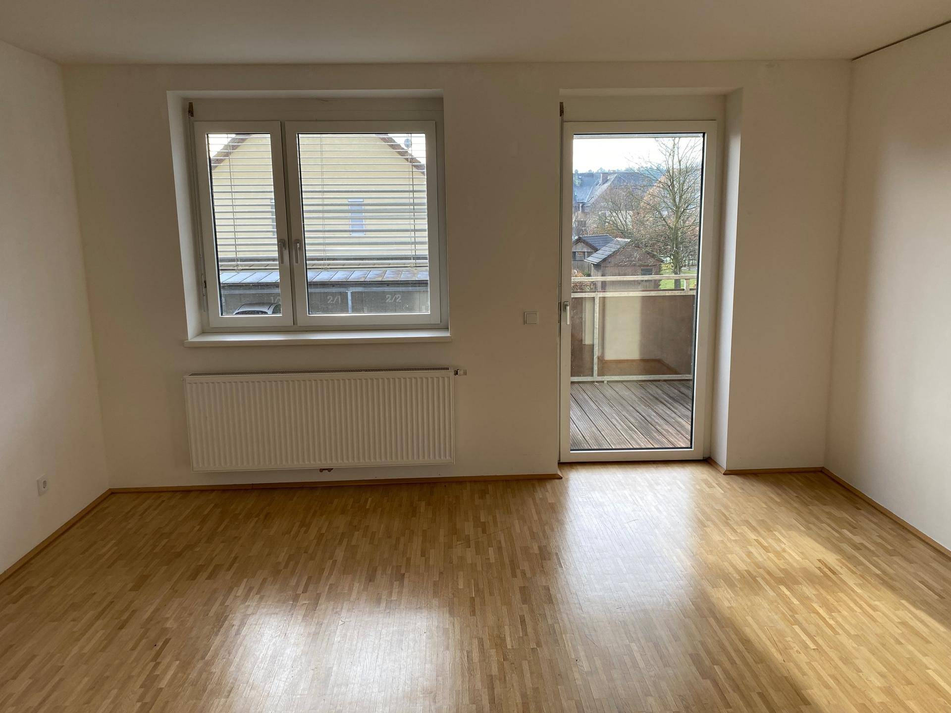 Geräumiger Wohnbereich mit Holzboden, Heizkörper und direktem Balkonzugang.