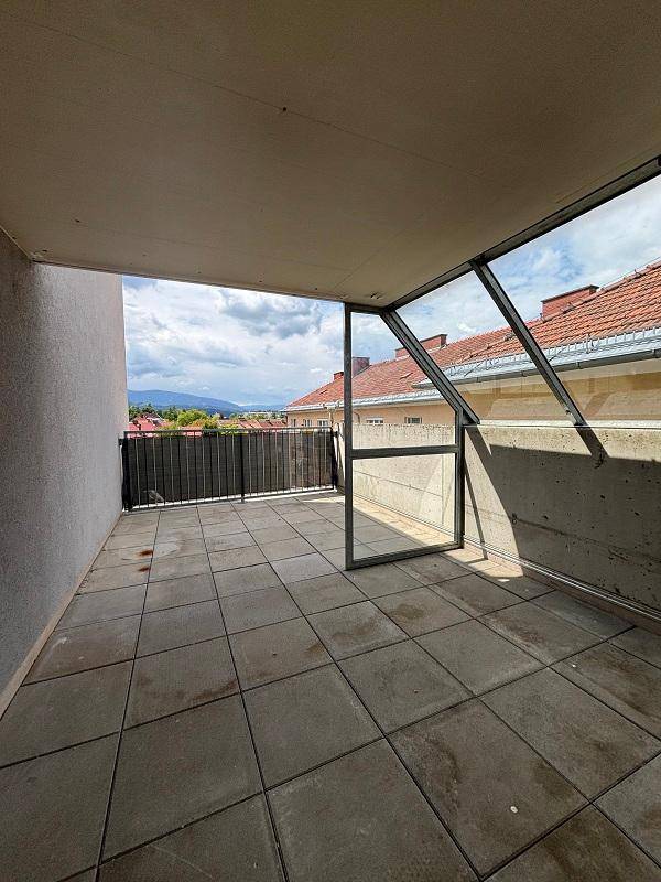 Geräumiger Balkon mit Fliesenboden, Blick über Dächer und auf die umliegenden Berge.