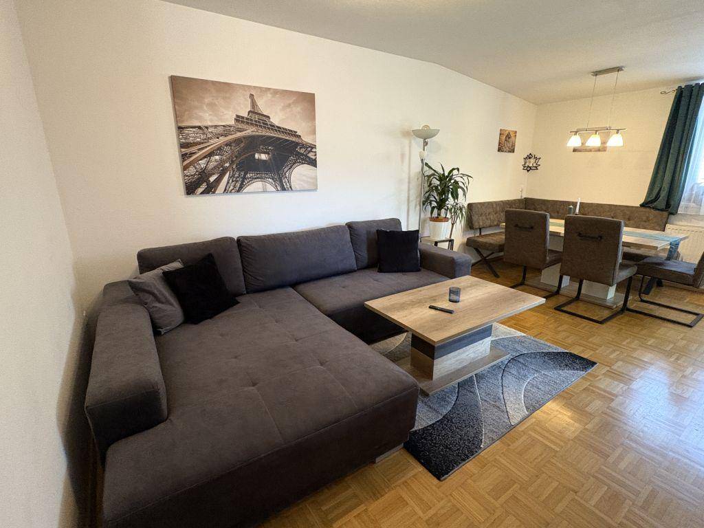 Heller Wohn-Essbereich mit Ecksofa, Couchtisch und Parkettboden, dekoriert mit einem Wandbild.
