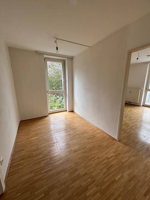 Helles Zimmer mit Parkettboden und großem Fenster, das viel Tageslicht hereinlässt.