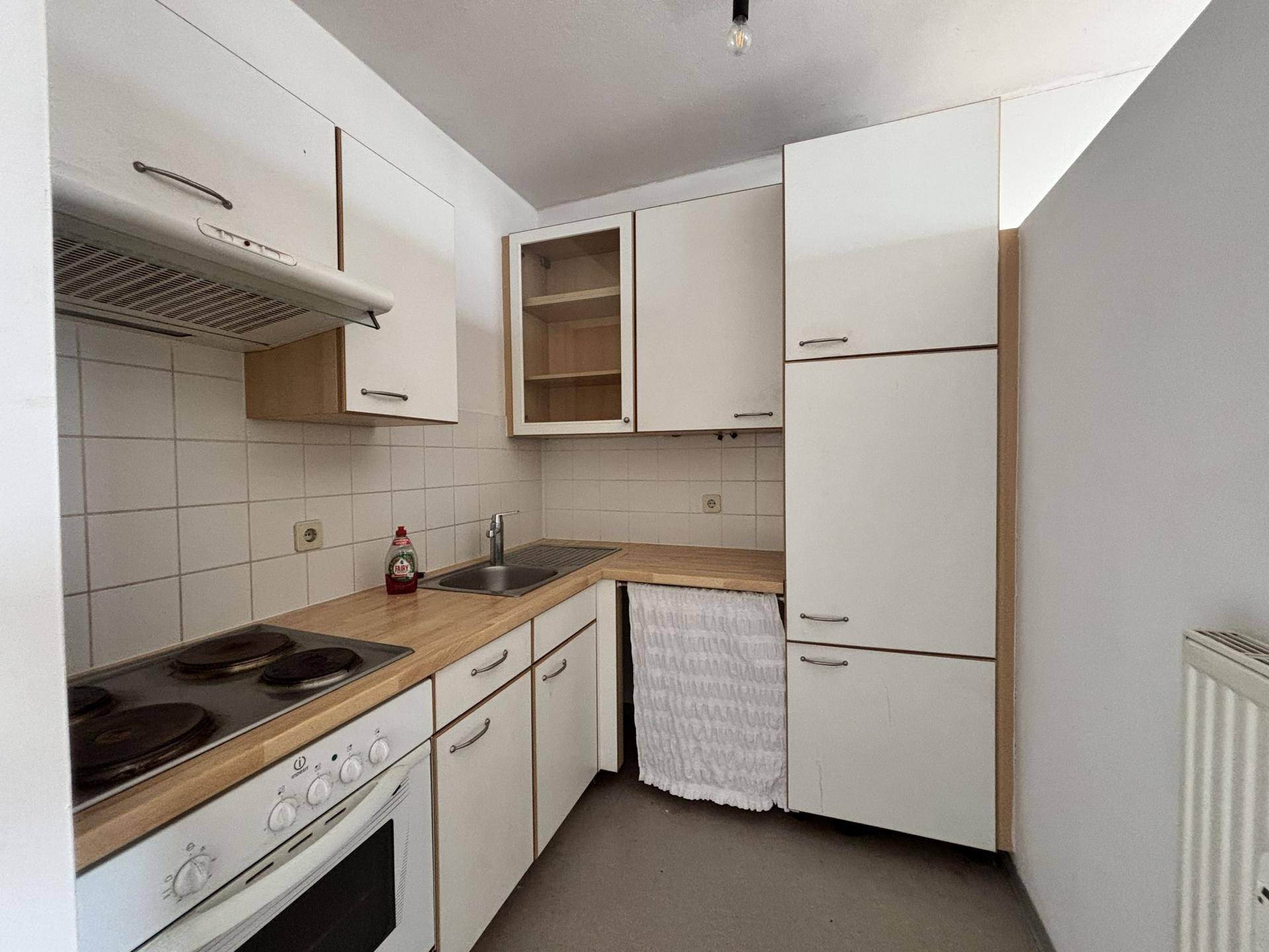 Kleine Küche mit weißen Schränken, Holz-Arbeitsplatte und integriertem Herd.