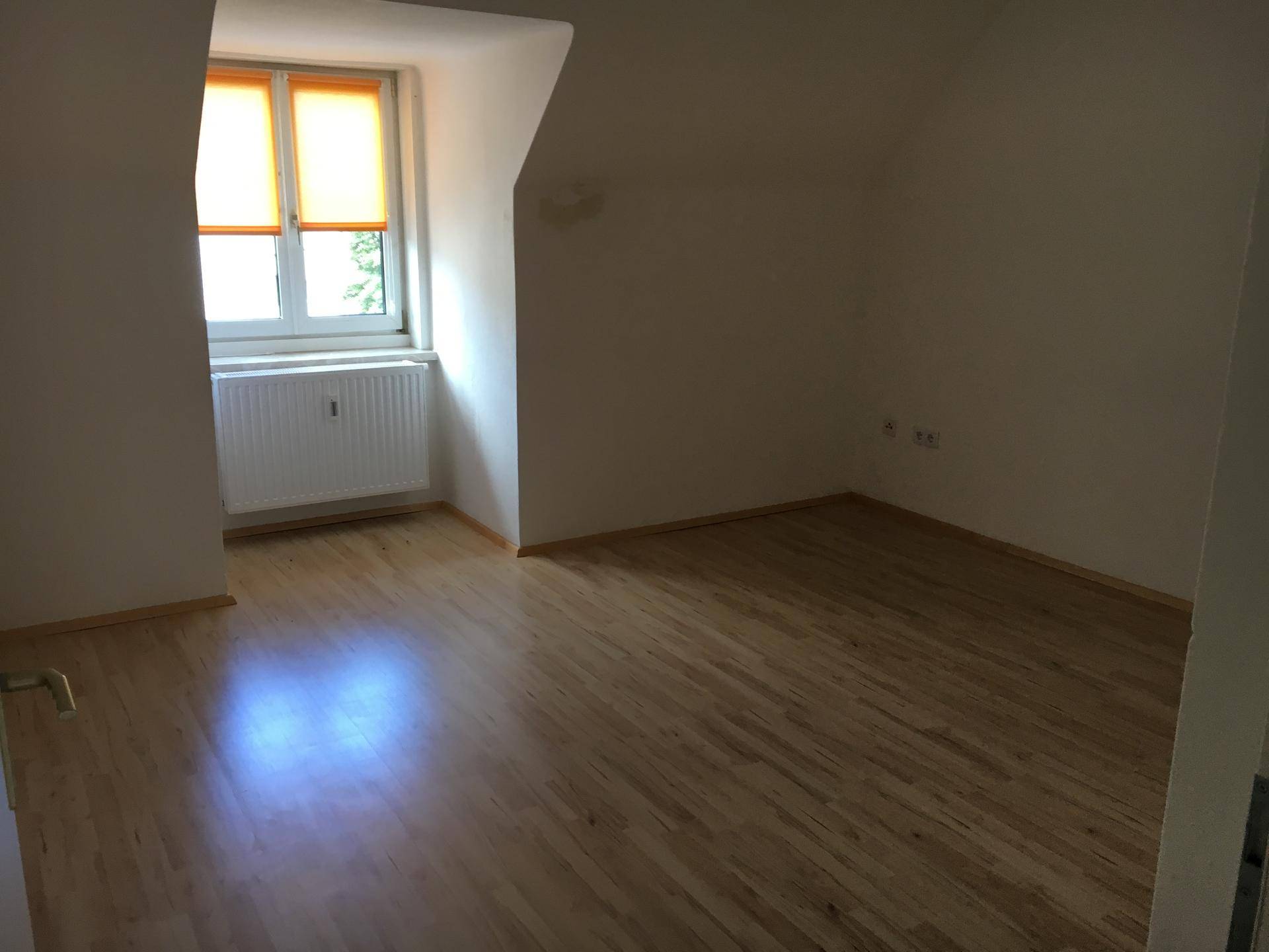Helles Zimmer mit Holzfußboden und einem Fenster mit orangefarbenem Rollo.