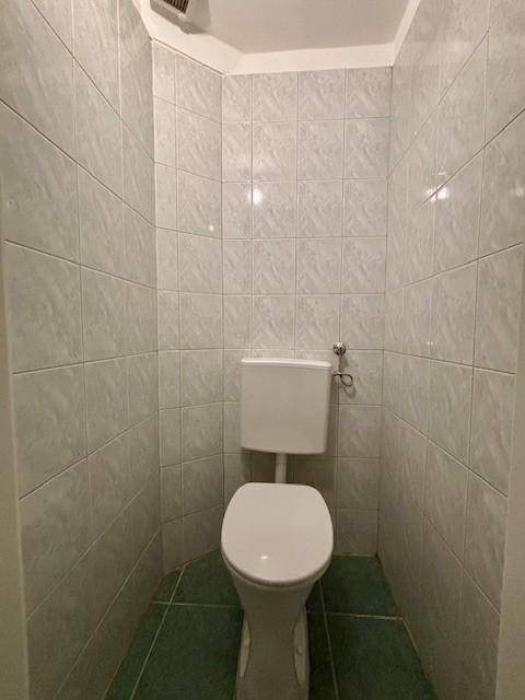 Kleiner WC-Raum mit hellen Fliesen an den Wänden und dunklem Fliesenboden.