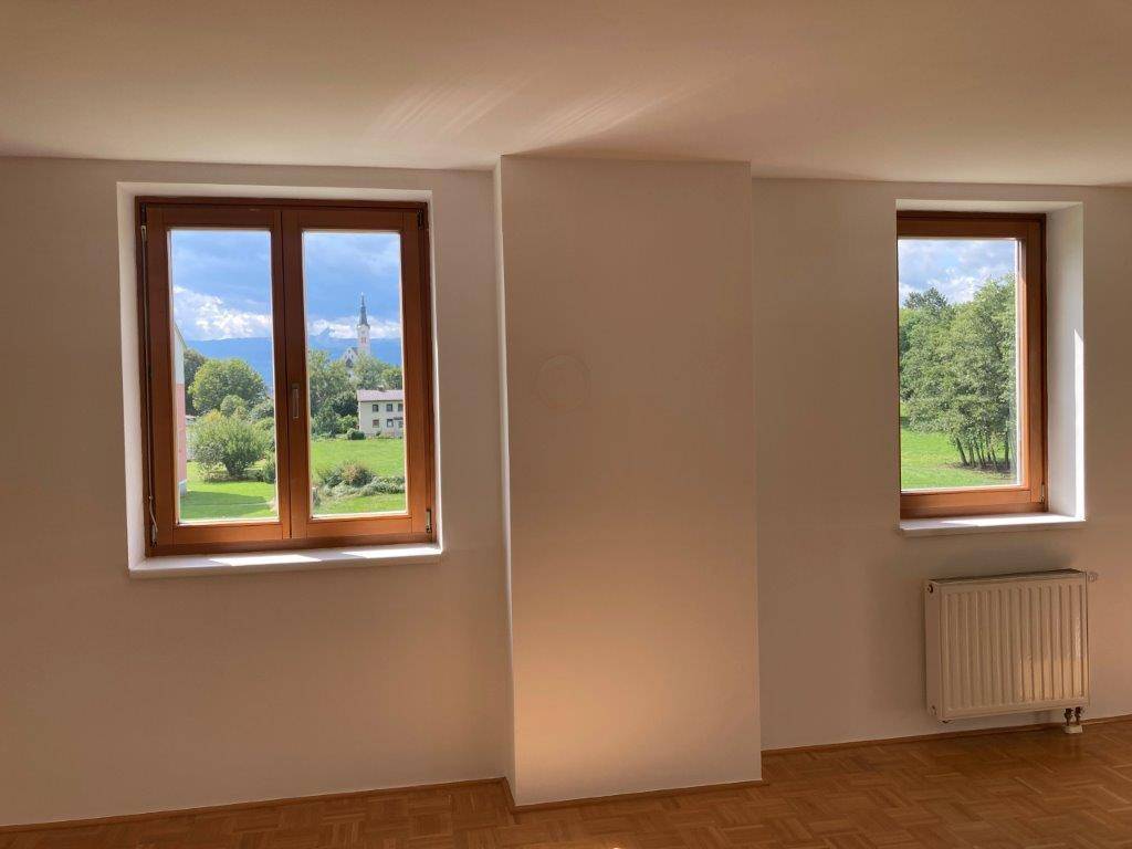 Heller Raum mit Parkettboden und weitem Blick auf grüne Landschaft und einen Kirchturm.