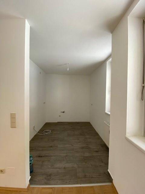 Leerer Raum mit neuem Laminatboden und weißen Wänden, bereit für die Einrichtung.