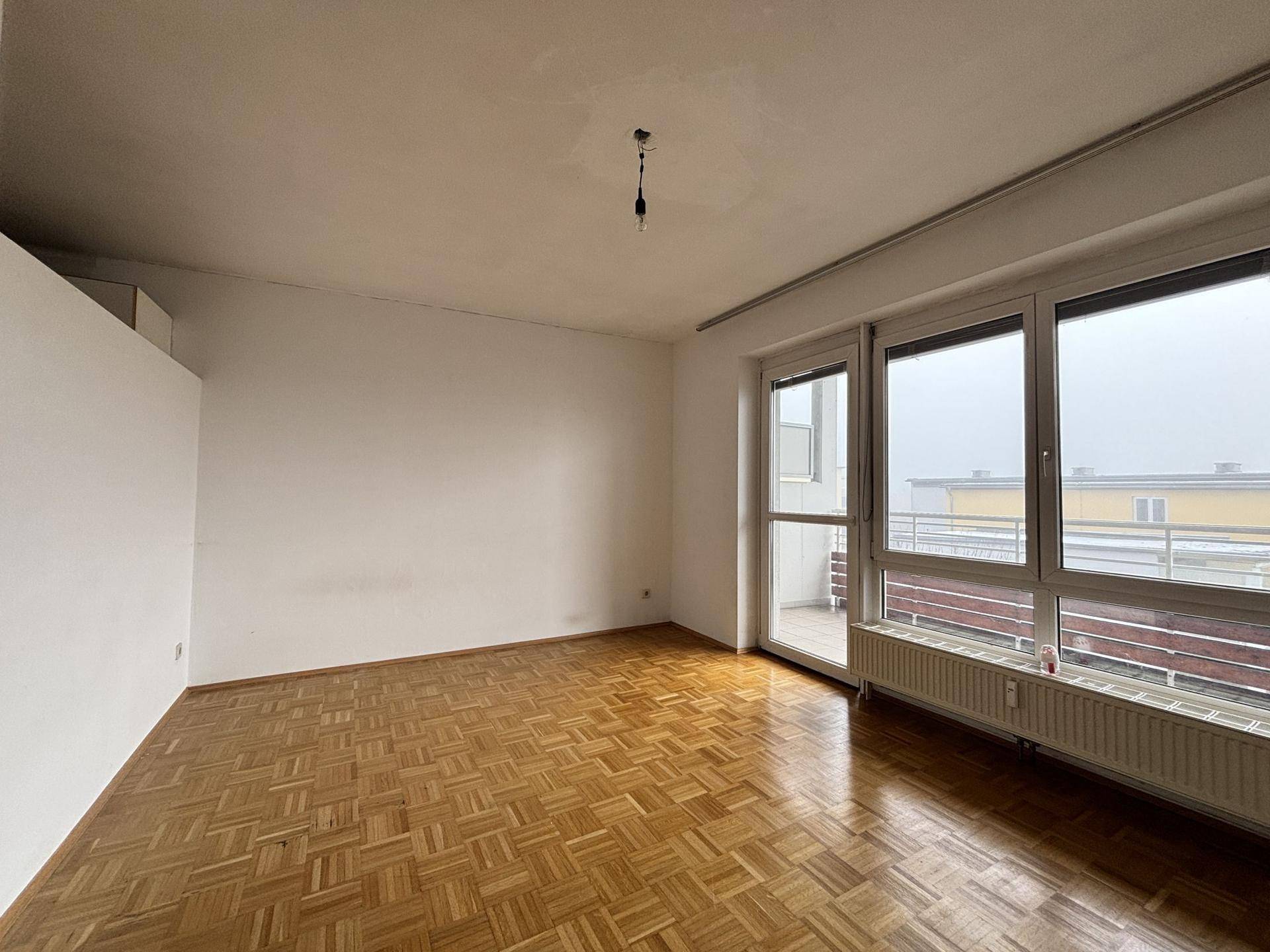 Helles Wohnzimmer mit Parkettboden und breiter Fensterfront, die viel Tageslicht hereinlässt.