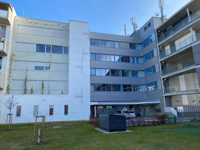 Moderne Gebäudefassade mit großen Fenstern, Balkonen und einer gepflegten Grünfläche im Vordergrund.