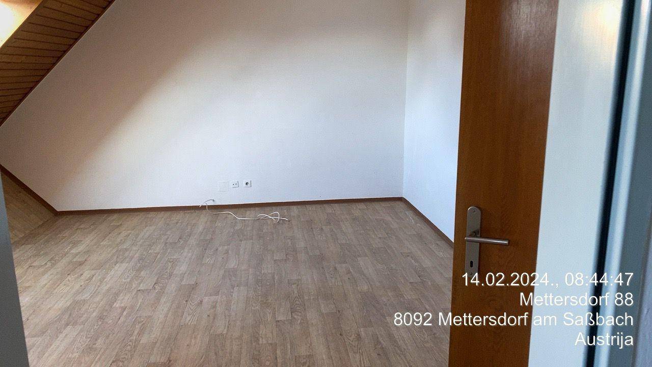 Leerer Raum im Dachgeschoss mit Laminatboden, weißen Wänden und schräger Deckenkonstruktion.