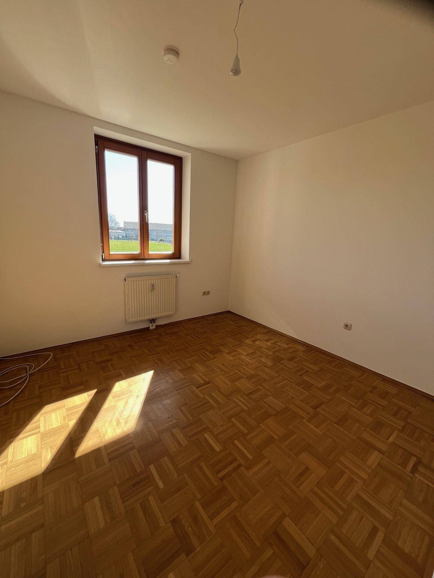 Helles Zimmer mit Parkettboden, großem Fenster und Heizkörper, ideal als Schlafzimmer oder Arbeitszimmer nutzbar.