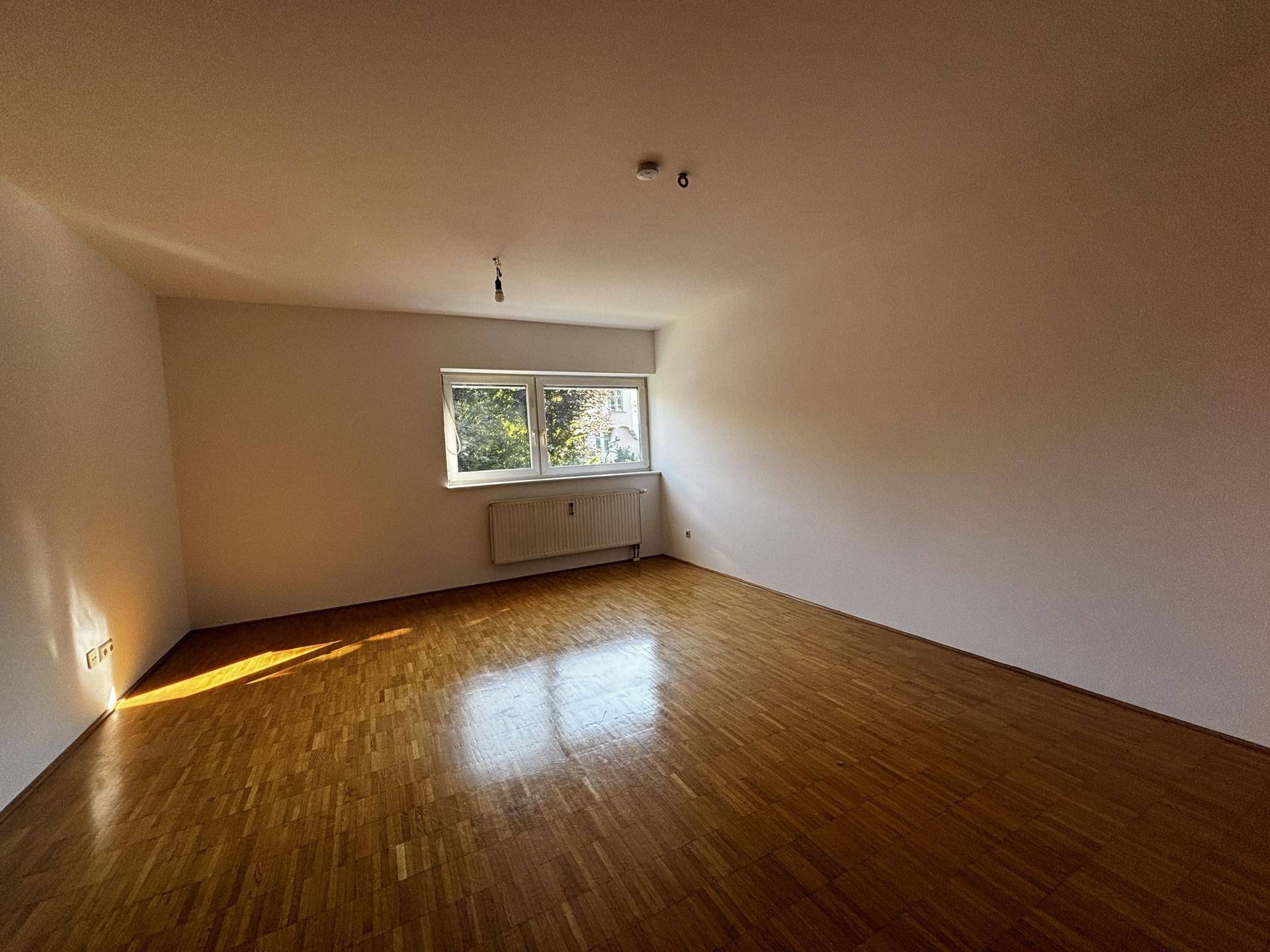 Geräumiges Zimmer mit Parkettboden, weißen Wänden und viel natürlichem Licht durch das Fenster.