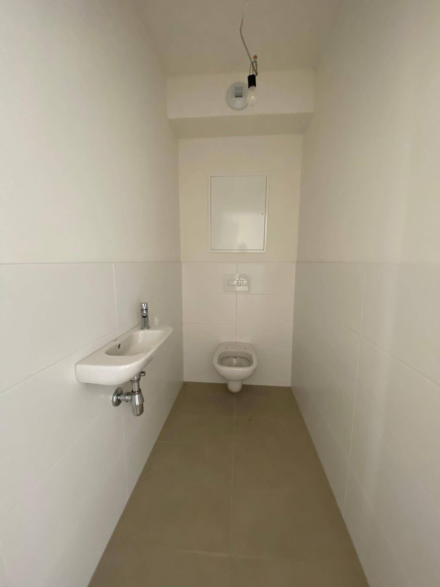 Separates WC mit wandhängender Toilette und kleinem Waschbecken, in schlichtem Design.