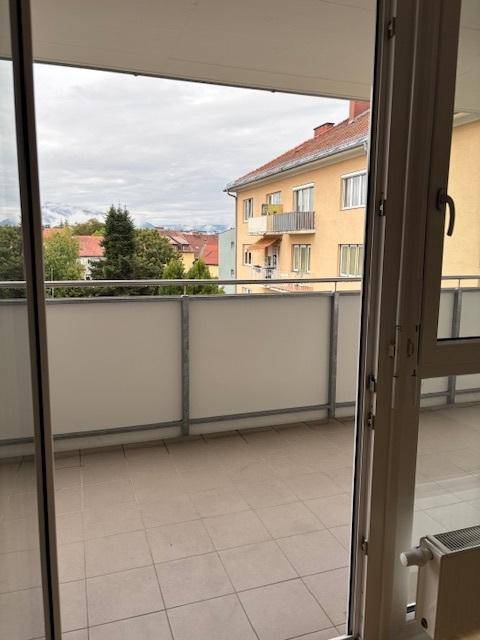 Balkon mit Fliesenboden und Blick auf die umliegenden Gebäude und grüne Bäume.