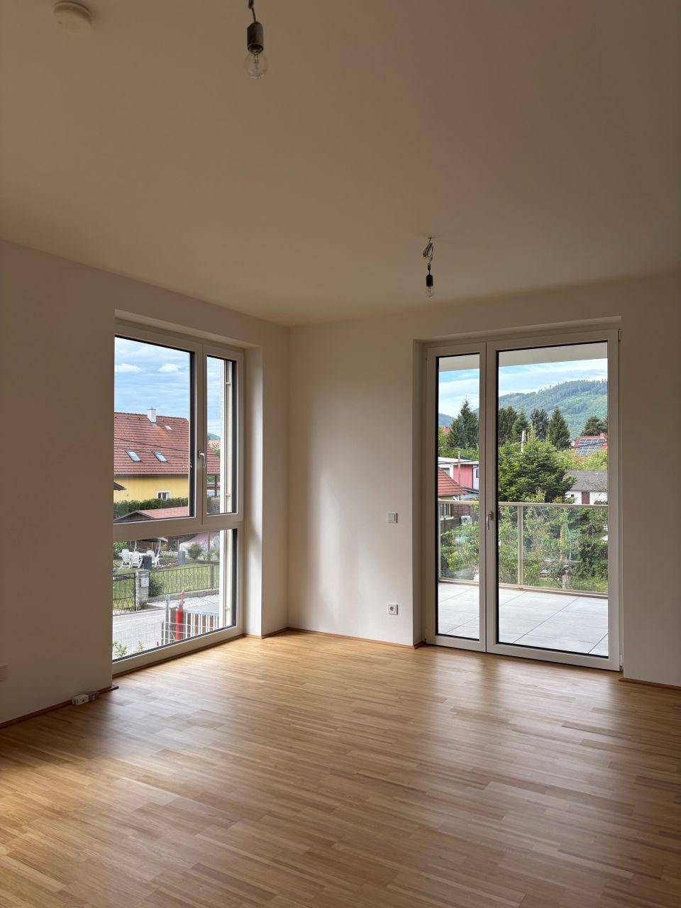 Helles Zimmer mit Parkettboden und Zugang zu einem Balkon oder einer Terrasse.