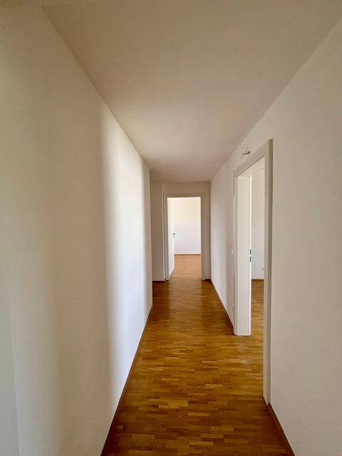 Langer, heller Flur mit Parkettboden und weißen Wänden, der verschiedene Zimmer verbindet.