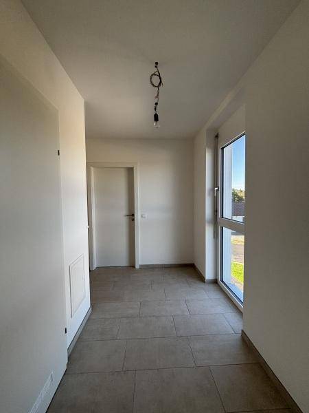Heller Flur mit Fliesenboden und einem Fenster, das Tageslicht in den Eingangsbereich bringt.