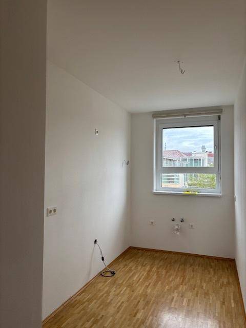 Kleiner Raum mit Parkettboden und Fenster, vorbereitet für Küchen- oder Hauswirtschaftsinstallationen.