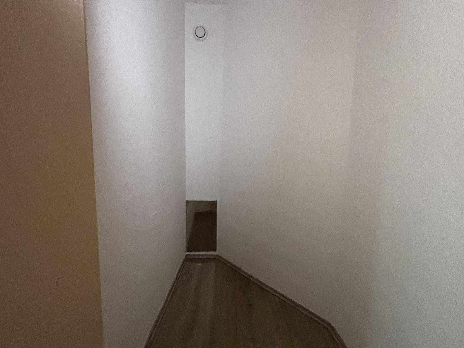 Schmaler, leerer Raum mit Laminatboden und weiß gestrichenen Wänden, möglicherweise ein Flur.