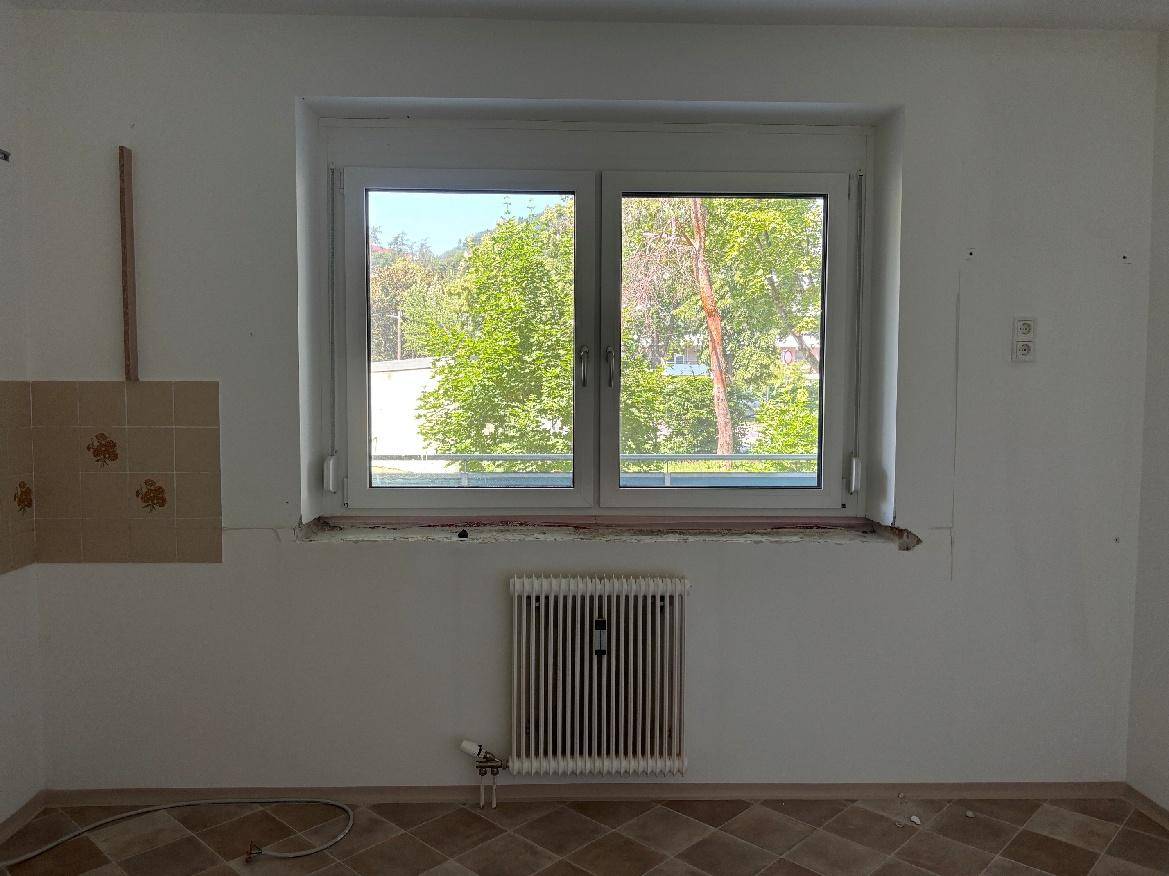 Leerer Küchenbereich mit Fenster und älteren Fliesen, bereit für eine neue Einrichtung.