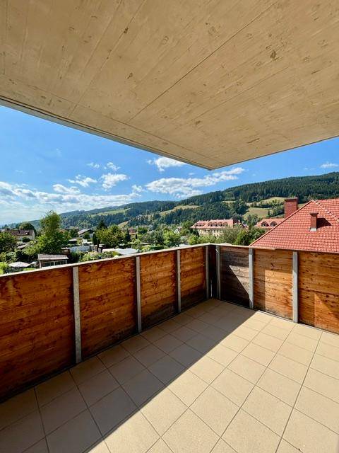 Großer Balkon mit Fliesenboden und Holzgeländer, bietet einen weiten Blick auf die grüne Landschaft.