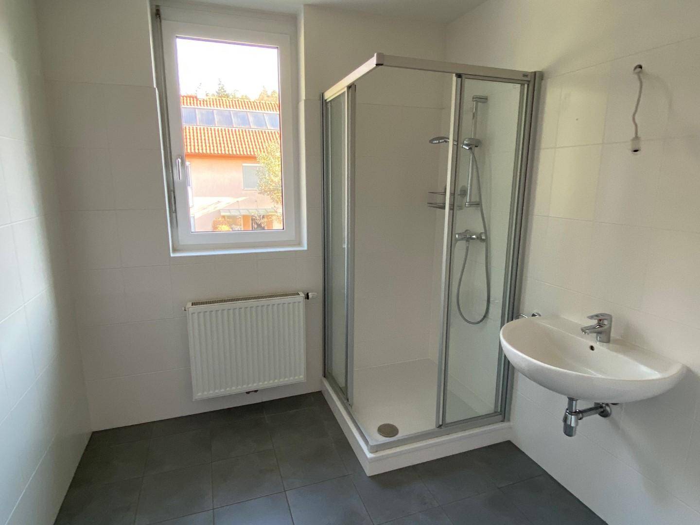 Modernes Badezimmer mit Duschkabine, Waschbecken und Fenster für natürliche Belüftung.