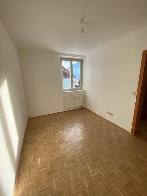 Leeres Zimmer mit Parkettboden und Fenster, das eine helle und freundliche Atmosphäre schafft.