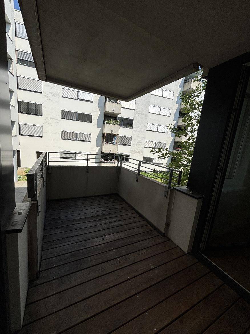 Geräumiger Balkon mit Holzfußboden und Blick auf umliegende Wohngebäude.