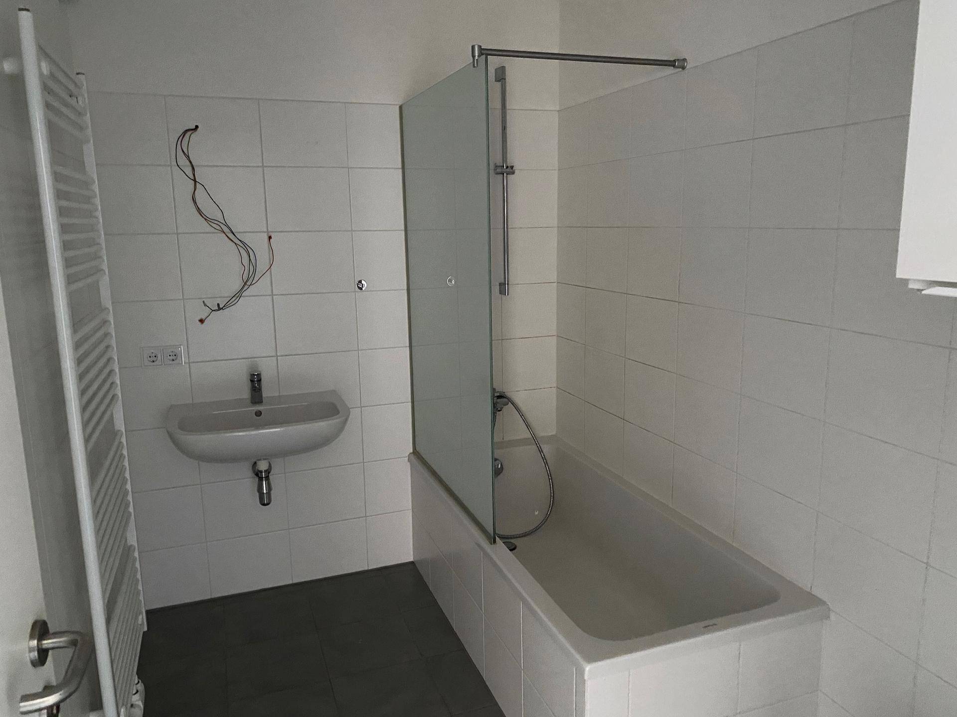 Badezimmer mit Badewanne, Duschabtrennung, Waschbecken und Handtuchheizkörper.