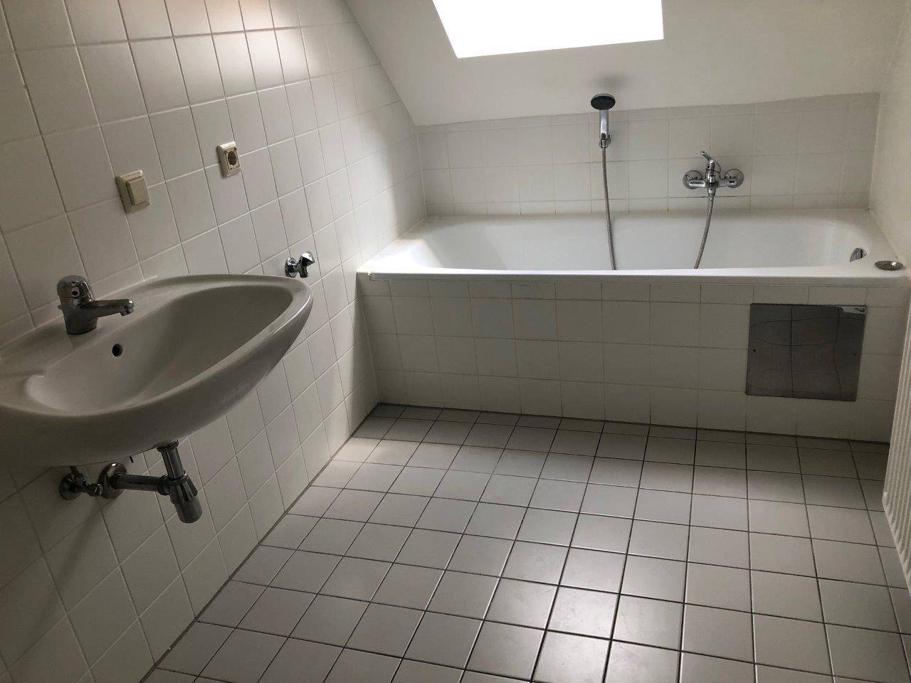 Helles Badezimmer mit weißen Fliesen, Badewanne und Dachfenster für natürliches Licht.