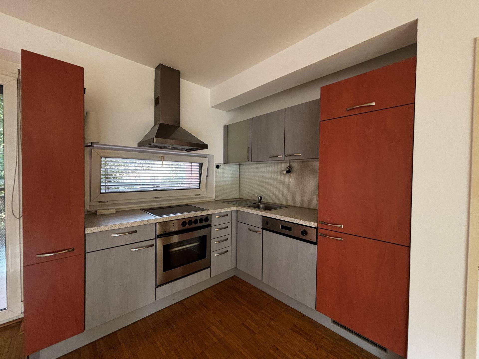 Moderne Küchenzeile mit roten und grauen Schränken, ausgestattet mit Herd, Backofen und Spülmaschine.