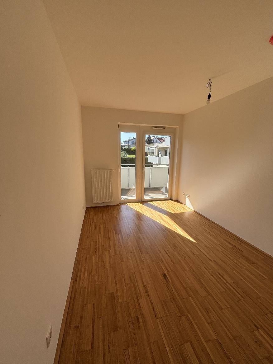 Schlafzimmer mit Holzboden, viel Tageslicht und direktem Zugang zum Balkon.