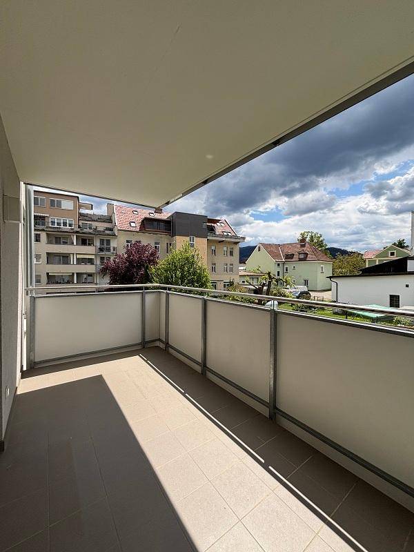 Geräumiger Balkon mit Fliesenboden und Blick auf die umliegenden Gebäude und Bäume.